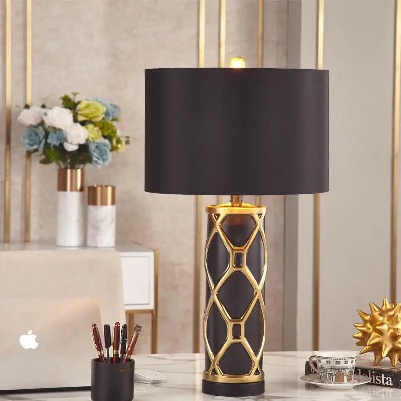 Decorative table lamp with black shade and gold base on a desk.