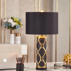 Decorative table lamp with black shade and gold base on a desk.