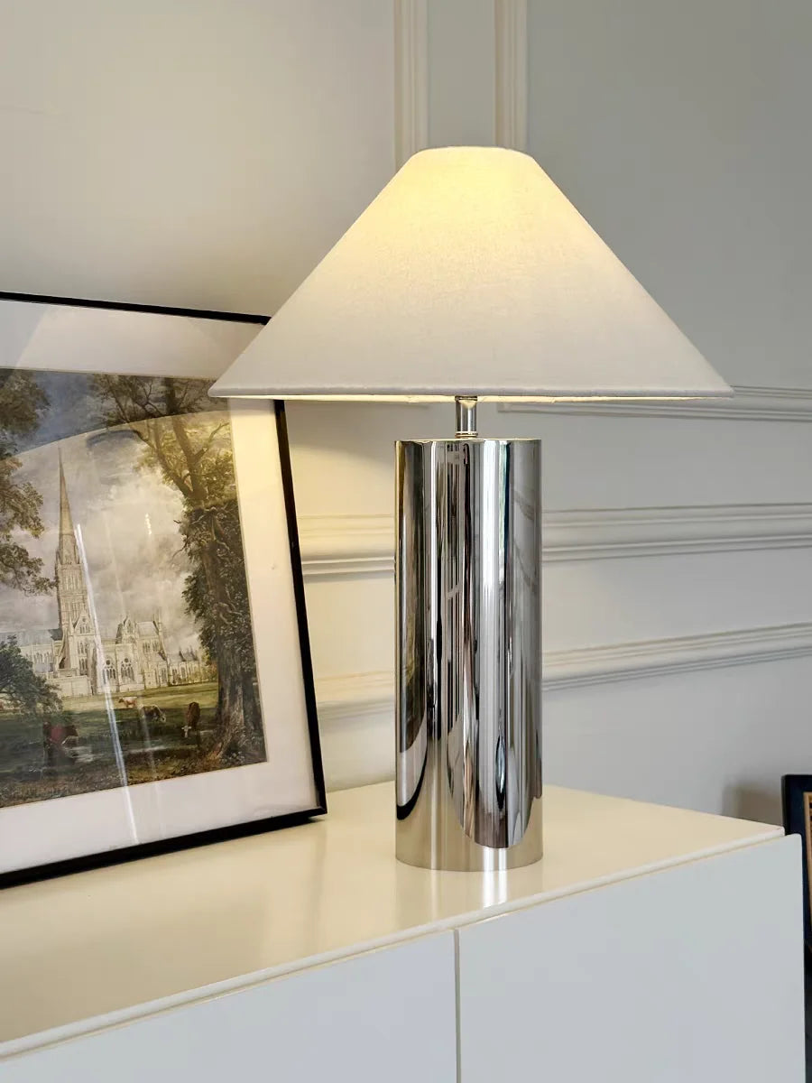 Table lamp with a white shade on a surface next to a framed picture.