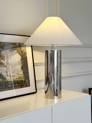 Table lamp with a white shade on a surface next to a framed picture.
