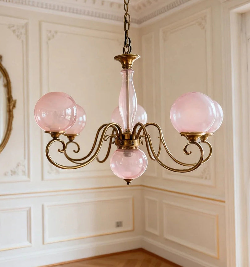 Close-up of a gold pendant light with pink glass globes and ornate arms, mounted in a room with ornate wall paneling.