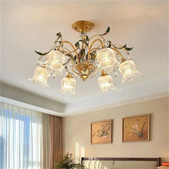 A smaller scale multi-arm gold chandelier with clear glass floral shades, mounted in a room with paintings on the wall.