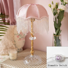 Decorative table lamp with pink fringed shade and dimmable switch inset on a checkered surface.