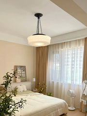 Cream decorative glass pendant light with a black chain hanging in a bedroom above a bed.