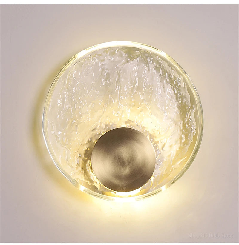 Decorative wall light fixture with a textured glass cover and brass finish on a neutral background.