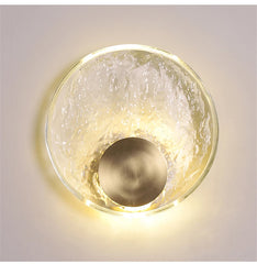 Decorative wall light fixture with a textured glass cover and brass finish on a neutral background.