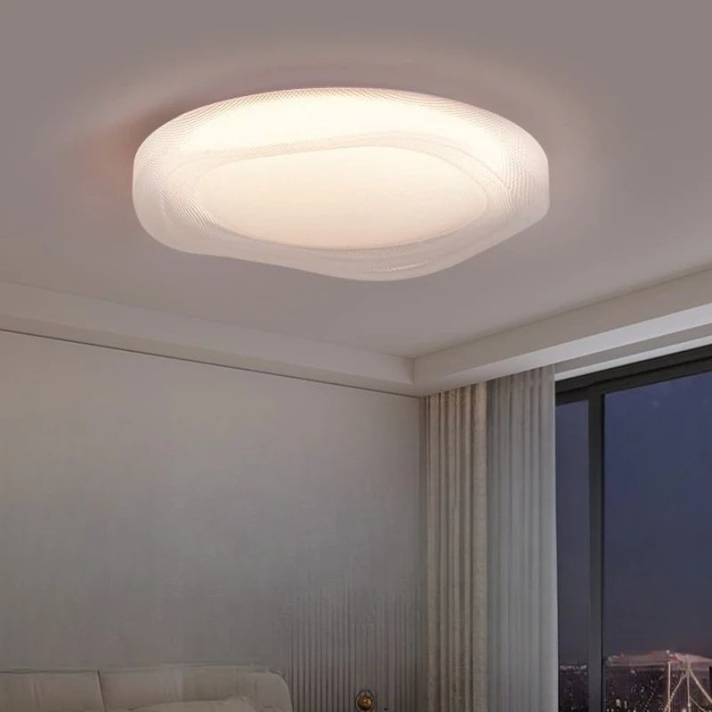 Side view of a modern white textured LED flush mount ceiling light installed on a ceiling above a bed.