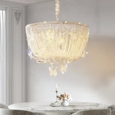 A luxurious polished chrome crystal waterfall pendant light with many crystal strands hanging over a marble-top dining table.