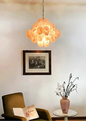 Chandelier hanging above a chair with a vase and book on a table, framed picture on the wall.