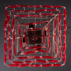 A tiered red glass chandelier hanging in a dimly lit room, casting a warm glow.