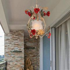 A gold floral pendant light with red rose accents displayed on a balcony with stone walls and a sliding glass door.