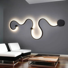 Black wave-shaped LED wall sconce with warm light mounted on a dark grey wall above white sofas.