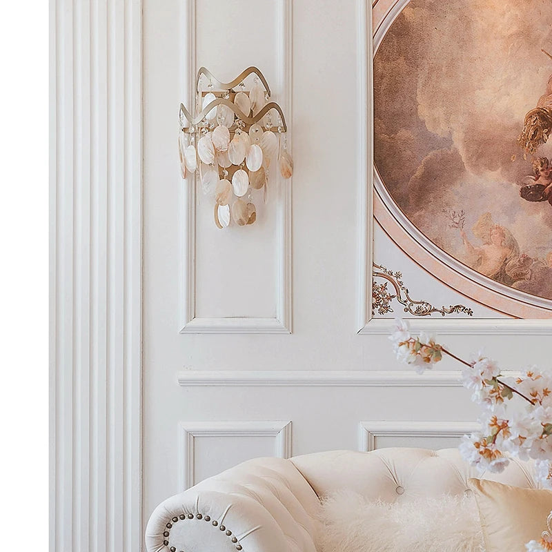 Gold wavy shell and crystal wall sconce mounted on a white paneled wall above a sofa.