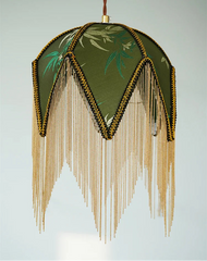 Decorative lamp with green floral design and gold fringe on a light gray background