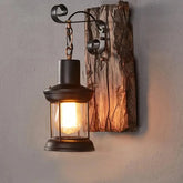 Black iron lantern wall sconce with a distressed wood backplate mounted on a gray wall.