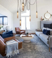 Modern living room with a gray sofa, brown armchair, and hanging pendant lights.