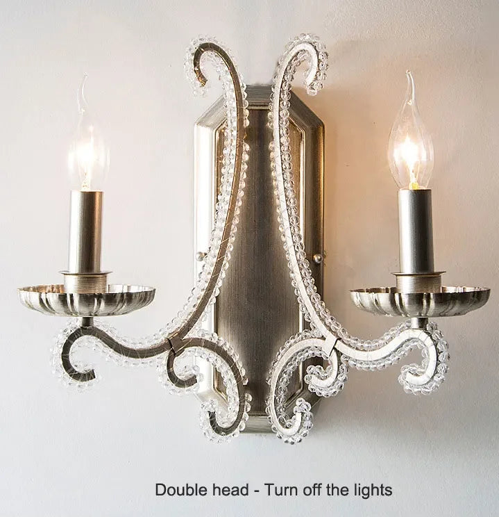 Decorative wall sconce with two candle-style light fixtures on a plain background.