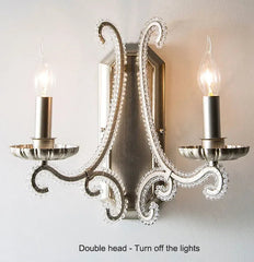 Decorative wall sconce with two candle-style light fixtures on a plain background.
