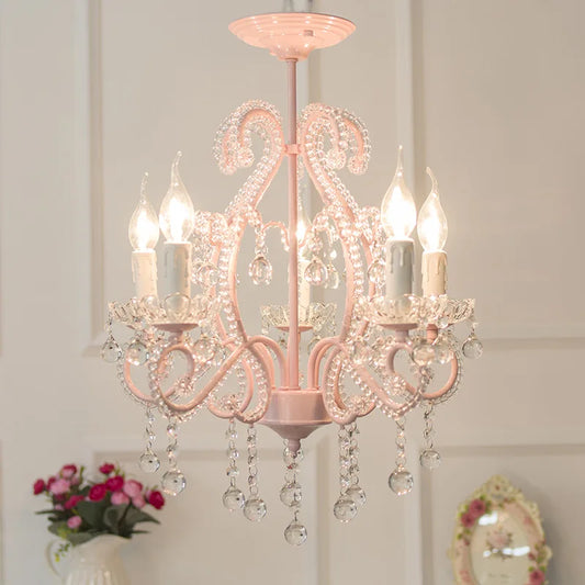 A pink candelabra-style chandelier adorned with clear crystal teardrop accents, illuminated and hanging from a ceiling.