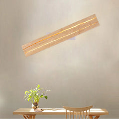 Wooden wall lamp on a plain wall with a table and plant in the foreground