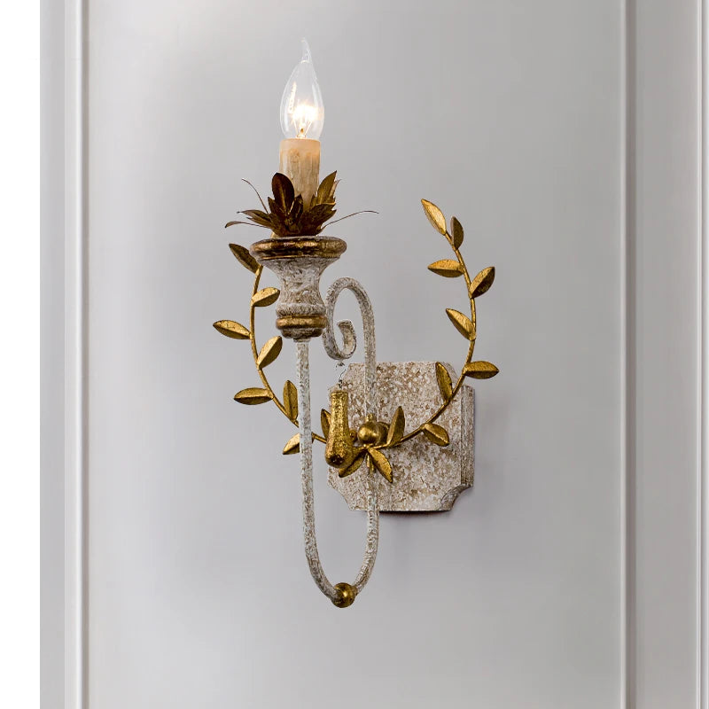 Close-up of a distressed gold floral leaf wall sconce showing intricate detailing and a candle-style light.