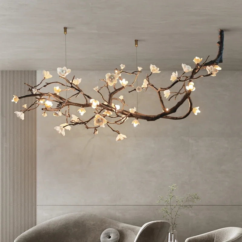 A view of a stylish copper-finished chandelier with a floral branch design and white blossoms, suspended from a ceiling in a contemporary room setting.