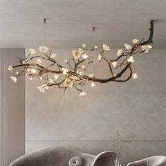 A view of a stylish copper-finished chandelier with a floral branch design and white blossoms, suspended from a ceiling in a contemporary room setting.