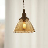 Amber pleated glass pendant light with a brass-toned fixture against a blurred window background.