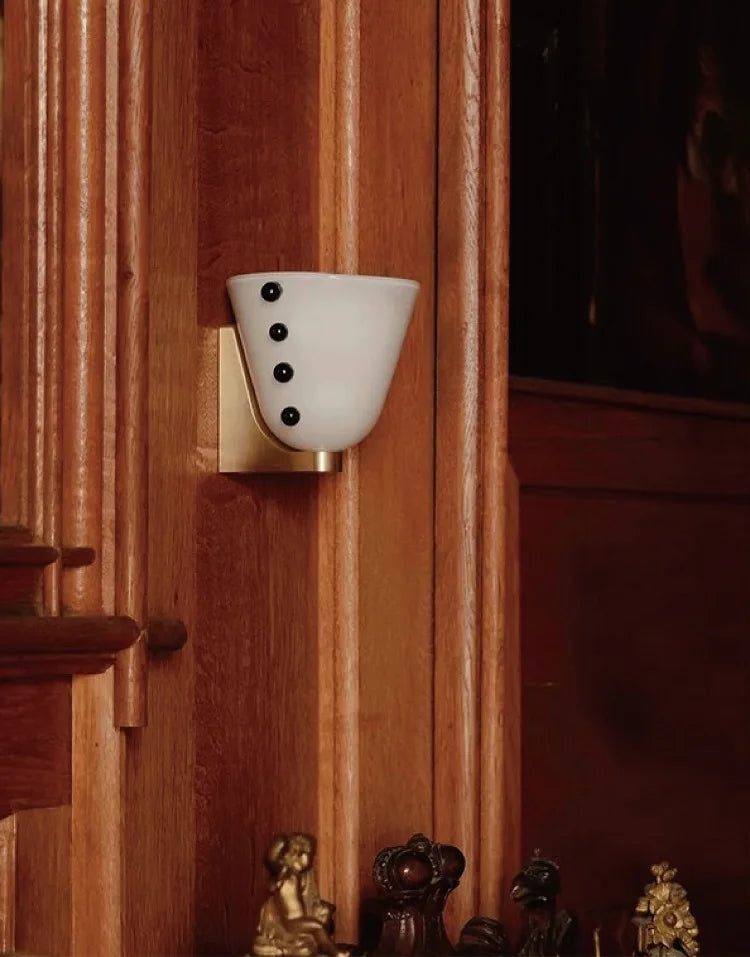 Decorative wall sconce with white shade and black buttons on a wooden wall.