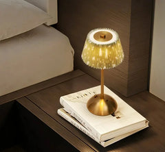 Decorative lamp with a gold base and white shade on top of books on a wooden surface.