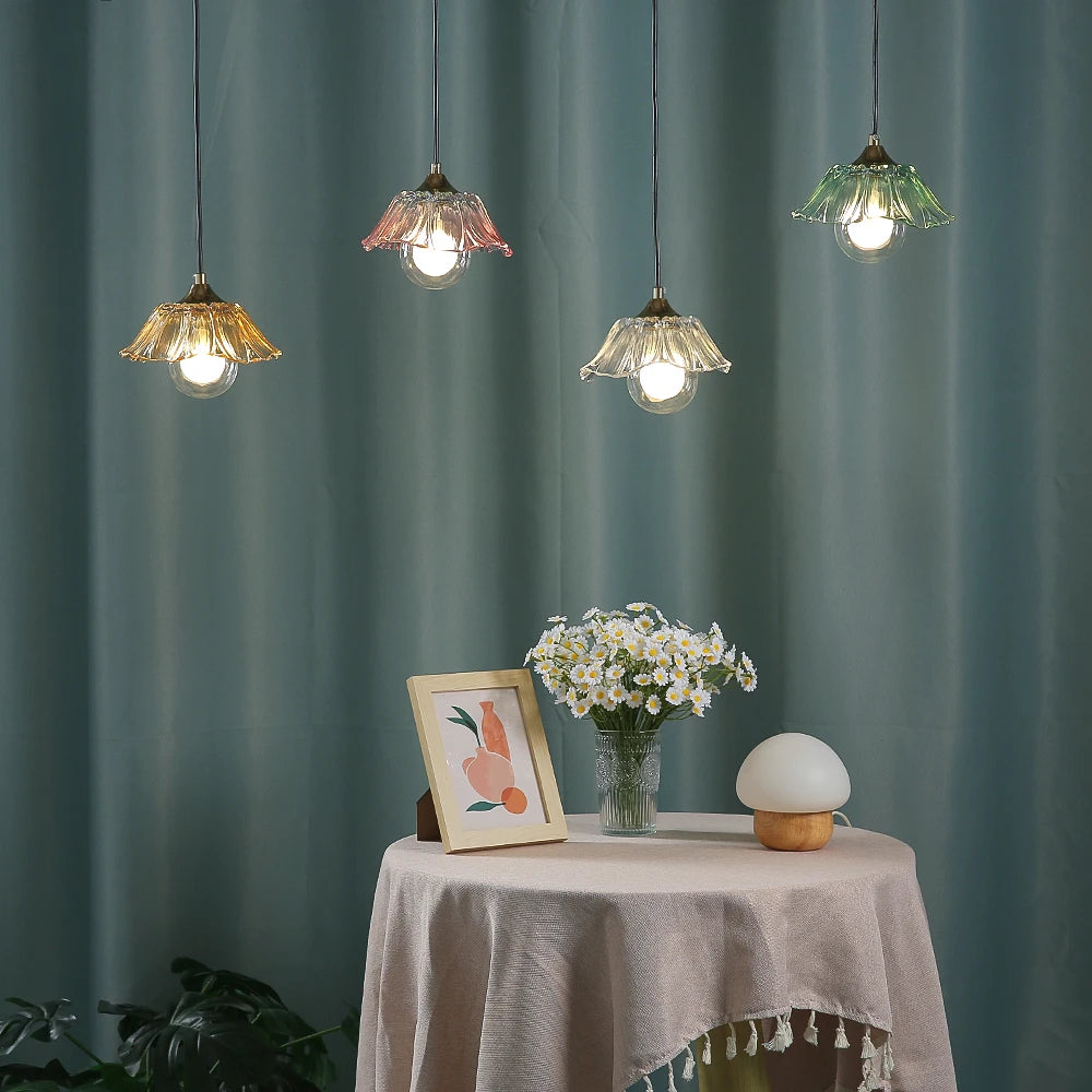 A round table with a vase of flowers and a framed picture, with four colorful glass pendant lights hanging in the background.