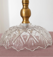 Clear glass lampshade with a brass base on a pink surface.