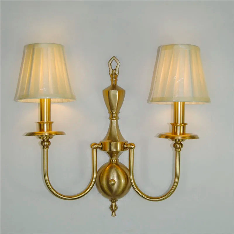 Gold wall sconce with two lampshades on a plain background