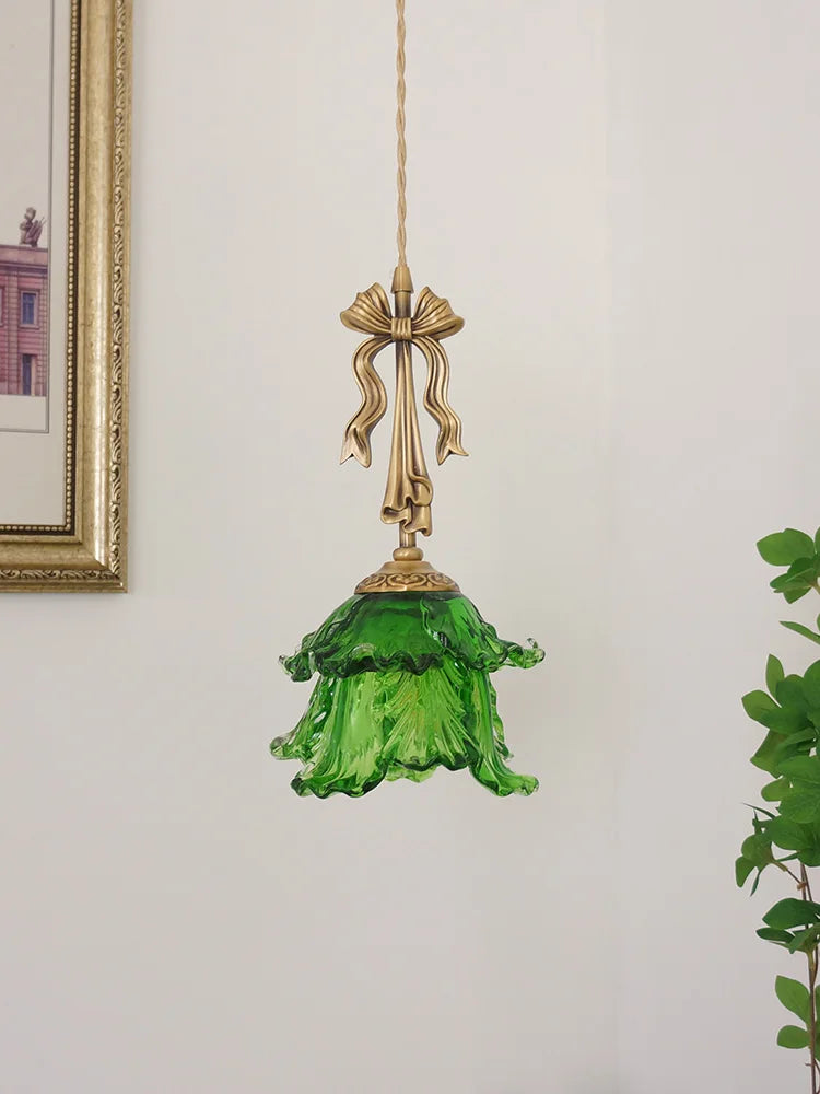 Green glass pendant light with gold fixture on a white wall.