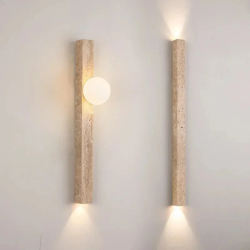 Close-up of a travertine stone wall sconce with a frosted globe emitting warm light.