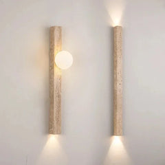 Close-up of a travertine stone wall sconce with a frosted globe emitting warm light.