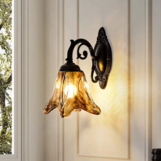 A single bronze glass bell wall sconce mounted on a cream-colored wall, with a window and greenery visible to the left.