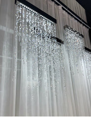 Crystal chandelier hanging from a ceiling with white curtains in the background