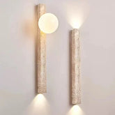 Two travertine stone wall sconces mounted on a plain wall, one with a frosted globe and warm light.