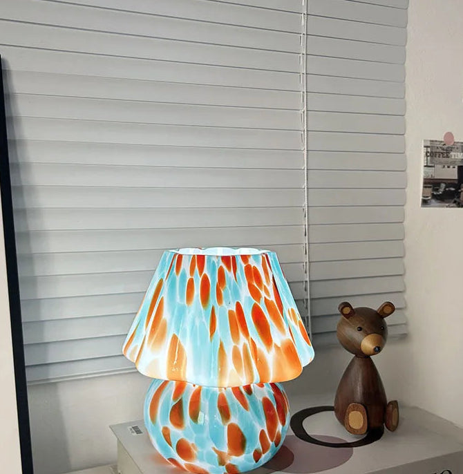 Colorful lamp with a pattern on a shelf next to a small bear figurine.