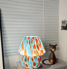 Colorful lamp with a pattern on a shelf next to a small bear figurine.