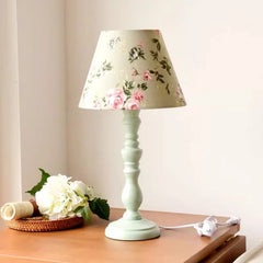 Floral-patterned lampshade on a light green base on a wooden surface.