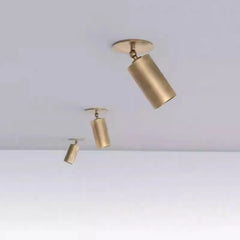 Three brushed brass cylinder spotlights of varying sizes mounted on a white ceiling, arranged diagonally.