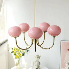 A gold chandelier with five pink globe-shaped glass shades, positioned above a white table.