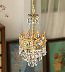 Gold chandelier with crystal accents hanging in a room with framed pictures on the wall.