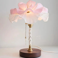 A close-up view of a white and pink petal-shaped table lamp with a brushed nickel base and pull chain.