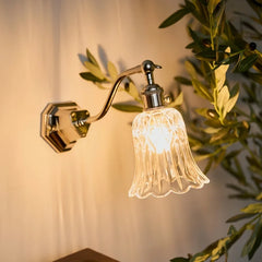A chrome wall sconce with a clear, tulip-shaped glass shade, mounted on a light-colored wall with soft lighting.