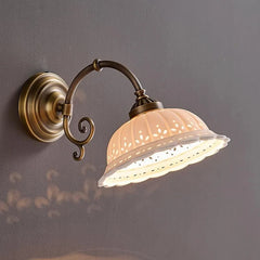 A close-up shot of a gold and white ceramic wall sconce with floral cutouts, mounted on a dark gray wall.