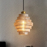 A tiered pendant light with ribbed glass shades and brass accents, illuminated against a textured gray wall.