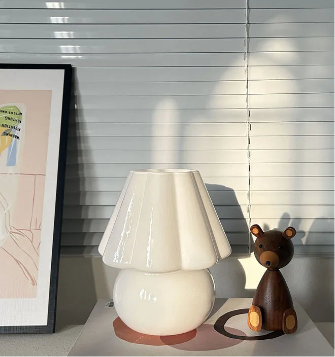 White lamp and brown bear figurine on a book with blinds in the background